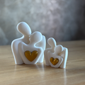 Two white figurines with gold hearts on a wooden surface